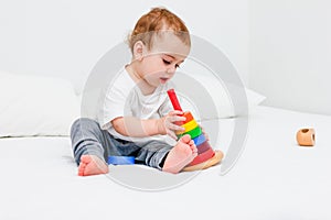 Pretty child 1 years old wearing white tshirt playing with wooden pyramid. Concept of wooden toy, children development