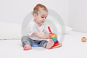Pretty child 1 years old wearing white tshirt playing with wooden pyramid. Concept of wooden toy, children development