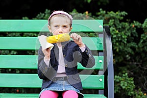 Pretty child girl eats a boiled corn outdoors