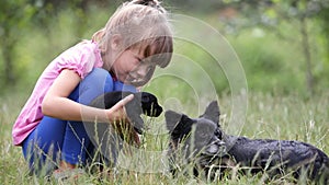 Pretty child girl playing with little puppy outdoors in summer.