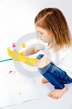 Pretty child girl smears yellow paint on hands