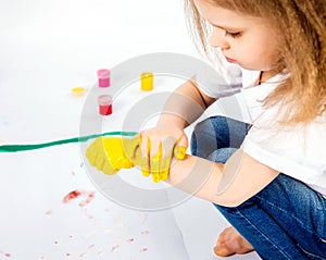 Pretty child girl smears yellow paint on hands