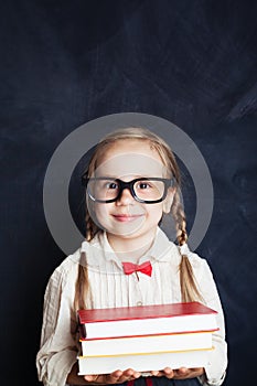 Pretty child girl with stack of books on chalkboard background.
