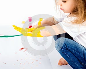 Pretty child girl smears yellow paint on hands