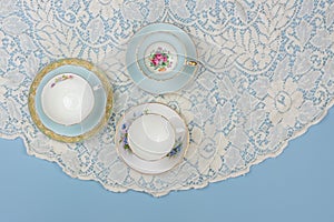Pretty china teacups on pale blue background with white lace