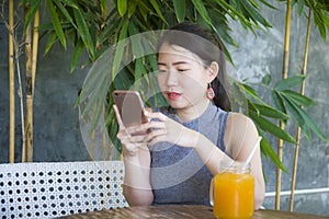 Pretty Chinese Asian woman using internet on mobile phone enjoying relaxed sending text social media chat at coffee shop outdoors