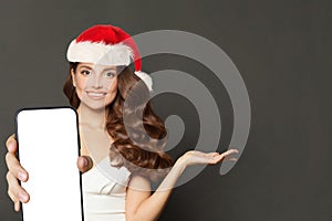 Pretty Christmas woman in Santa hat showing smartphone with empty blank display screen and holding open hand palm on black