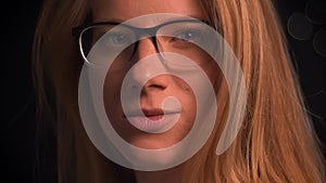 Pretty close-up face of spectacled caucasian blonde woman, turning her head at camera with serious glance, artistic