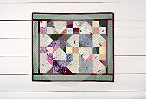Pretty and Colorful Small Quilt Hanging, or laying, Centered on Rustic White Painted Wood Board wall Background.