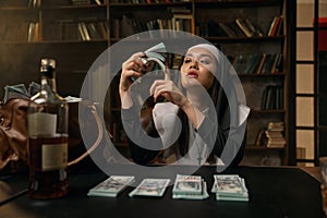 Pretty confident woman in nun dress sitting at table with money stacks photo