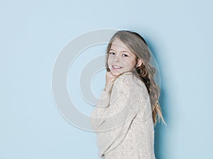 Pretty and cool 9 year old girl with brown wool sweater posing in front of blue background
