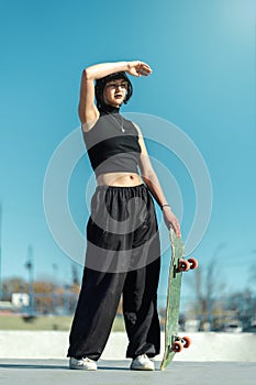 Pretty cool skater girl with eye glasses posing with her skate board towards the sunlight