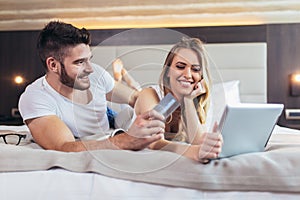 Couple with credit card and digital tablet lying in bed and doing online shopping