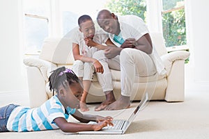 Pretty couple sitting on couch and their daughter using laptop