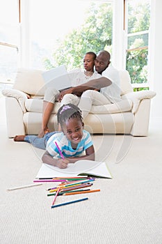 Pretty couple using laptop on couch and their daughter drawing