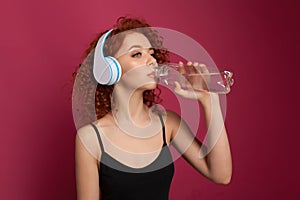 Pretty healthy young woman drinking pure mineral bottled water on a pink background