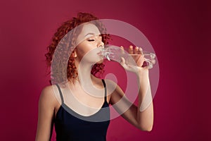 Pretty healthy young woman drinking pure mineral bottled water on a pink background