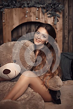 Pretty cute brunette girl posing with big teddy bear on the floor in cozy comfortable interior home.