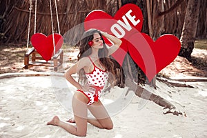 Pretty cute girl model in pinup style swimwear posing on white sand, over hearts. Maldives concept