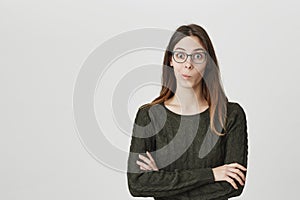 Pretty dark-haired caucasian female model in spectacles with rounded lips, looks in astonishment at camera, has puzzled