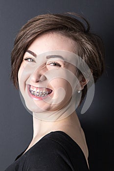 pretty dark haired teenage girl with braces smiling on a black background