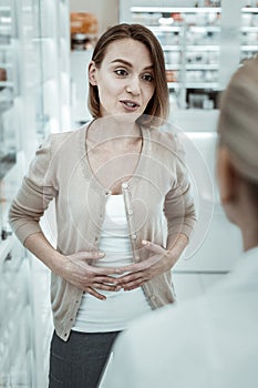 Pretty dark-haired woman sharing with druggist her stomach ache problems