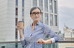 Pretty dear relaxing girl is holding a brown cup of coffee in her hand and looking at side with a slight smile