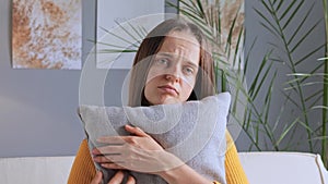 Pretty depressed woman with brown hair feeling depress and sadness being lonely looking at camera with unhappy face hugging pillow