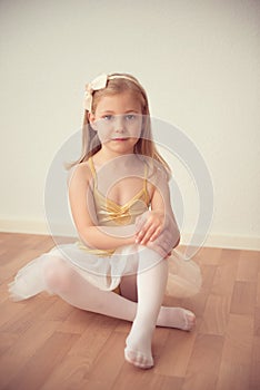 Pretty diligent ballet girl sitting in white tutu at dance studio photo