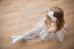 Pretty diligent ballet girl sitting in white tutu at dance studio photo