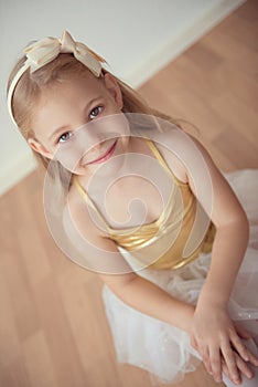 Pretty diligent ballet girl sitting in white tutu at dance studio