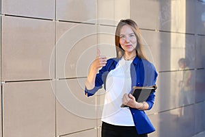 Pretty diligent student girl looks straight at camera, holds thumbs up, shows gesture indicating cool, smiling and holds