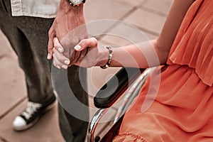 Pretty disabled girl sitting in wheelchair and holding hand of boyfriend