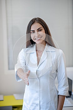 Pretty doctor in a lab coat smiling and stretching her arm