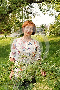 A beautiful elderly woman in flaxen clothes stands tranquilly in her green garden photo