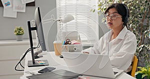 Pretty elegant women in glasses with Asian Korean beauty sits in office of company with headphones microphone on ears in