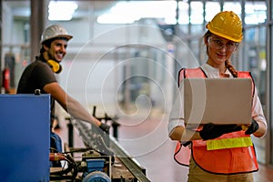 Pretty engineer or technician or worker woman hold the laptop and her co-worker stand and smile in the background and they work