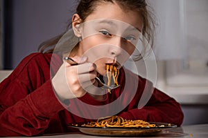 Pretty enjoying grimacing kid girl eating tasty spaghetti on the dinner on the home kitchen. Closeup