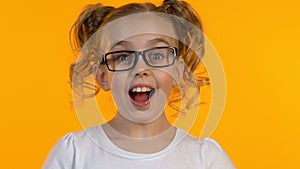 Pretty erudite girl in glasses having idea, close-up, isolated yellow background