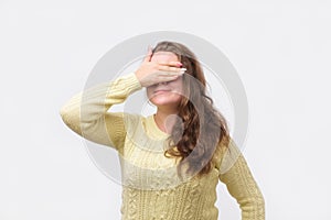 Pretty european girl in yellow sweater closing her eyes with hand, having happy expression