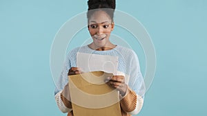 Pretty excited african american girl in sweater emotionally opening envelope with exams results over colorful background