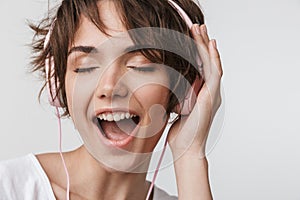 Pretty excited happy woman posing isolated over white wall background listening music with headphones