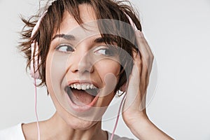 Pretty excited happy woman posing isolated over white wall background listening music with headphones