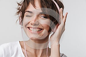 Pretty excited happy woman posing isolated over white wall background listening music with headphones