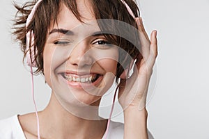 Pretty excited happy woman posing isolated over white wall background listening music with headphones