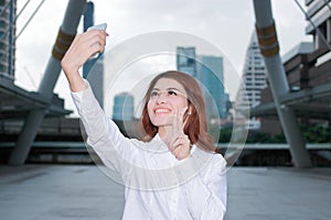 Pretty face young Asian woman taking a selfie photo at urban city background. Selective focus and shallow depth of field.