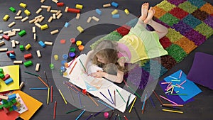 Pretty female child lying on the floor and drawing with color pencils on paper