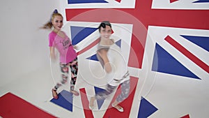 Pretty female dancers look at camera and move in white studio with big UK flag