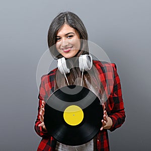 Pretty female DJ with headphones and vinyl against gray background