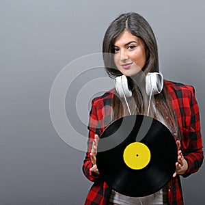 Pretty female DJ with headphones and vinyl against gray background